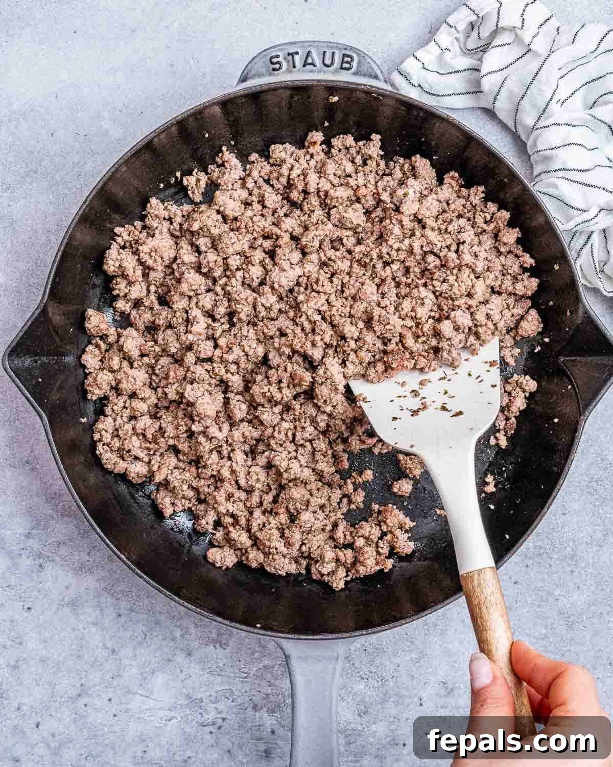 Ground beef in a cast iron skillet stirred by a spatula. 