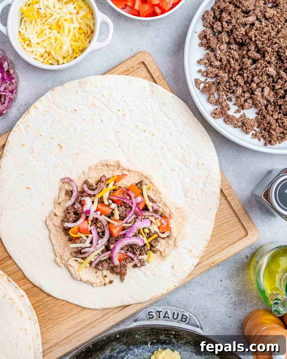 Hummus, sausage, onions, tomatoes on a large flour tortilla.