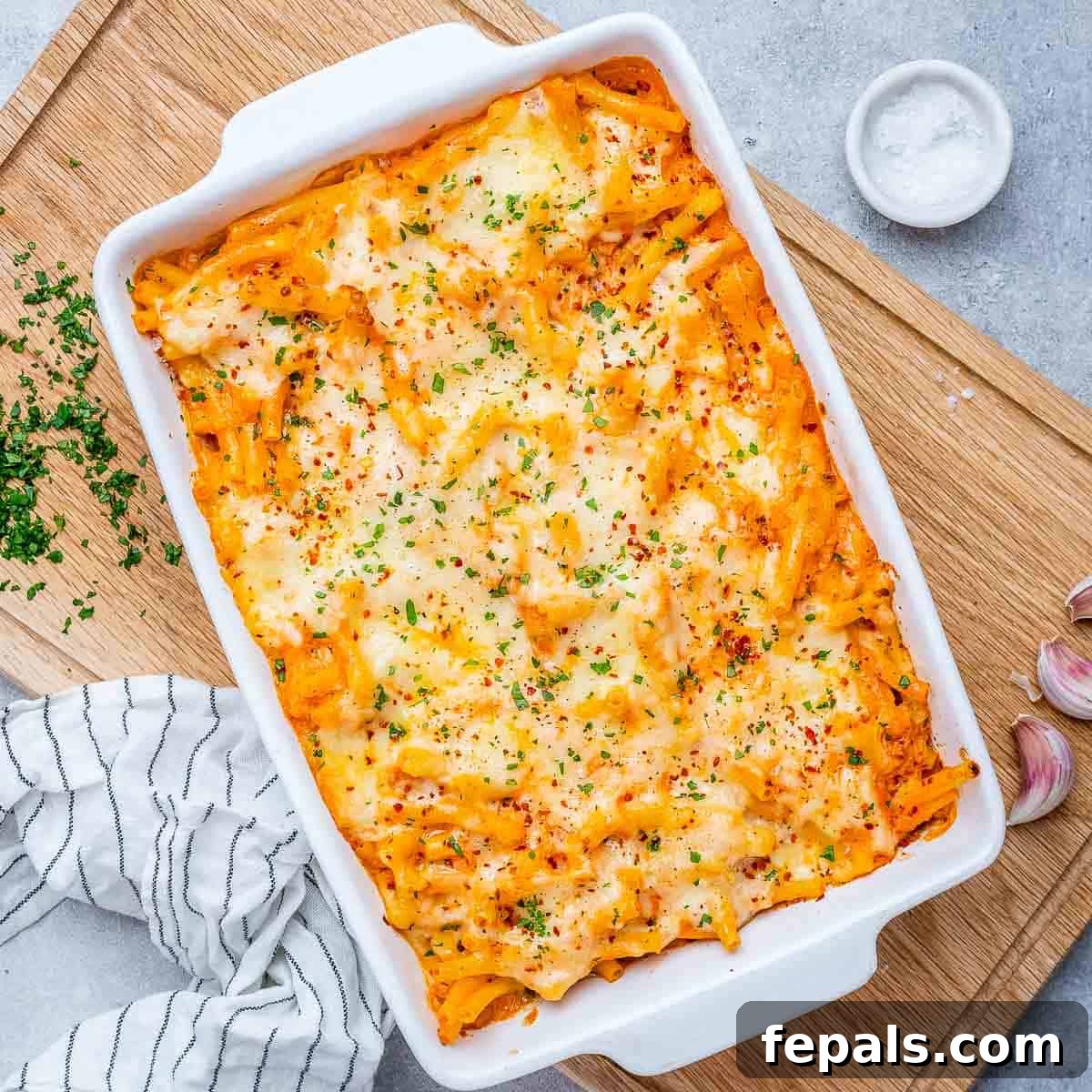 Ultimate Cheesy Baked Ziti 2 A large white baking dish filled with golden-brown baked ziti, topped with glistening melted cheese and hints of red tomato sauce.