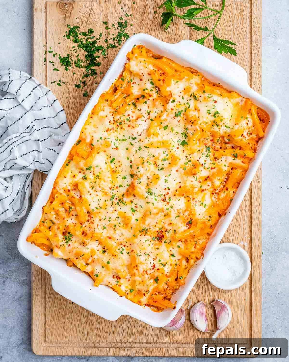 Ultimate Cheesy Baked Ziti 11 A pristine white baking dish showcasing a generous serving of baked ziti pasta, resting on a rustic brown cutting board.