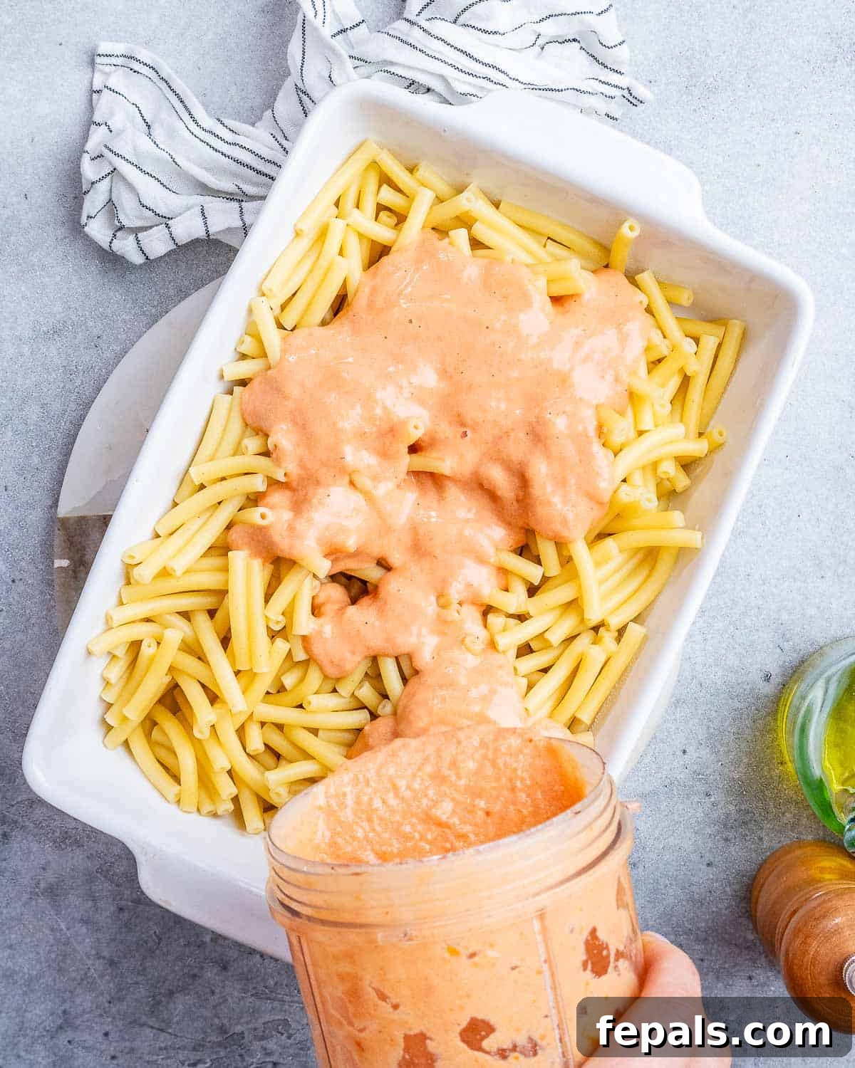 Ultimate Cheesy Baked Ziti 8 Rich, red sauce being poured generously over a bed of cooked ziti pasta in a white casserole dish.