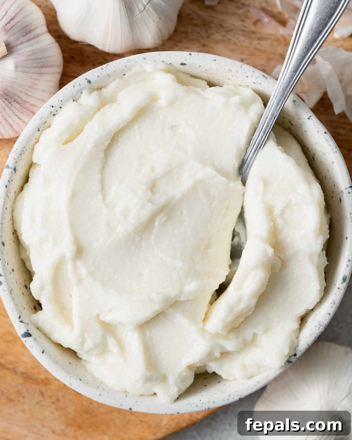 Fluffy Lebanese Garlic Dip 12 A spoon resting in a bowl of creamy Lebanese garlic sauce, perfectly smooth and ready to scoop.