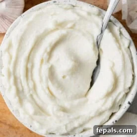 Fluffy Lebanese Garlic Dip 14 A round bowl with fluffy garlic sauce dip with a spoon in it.