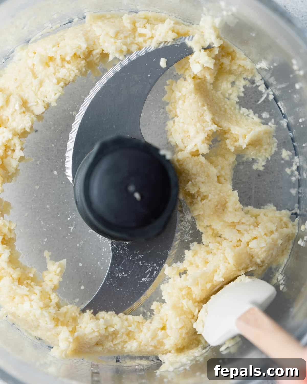 Fluffy Lebanese Garlic Dip 5 Finely chopped garlic and salt being blended in a food processor, with a spatula scraping down the sides to ensure even processing.