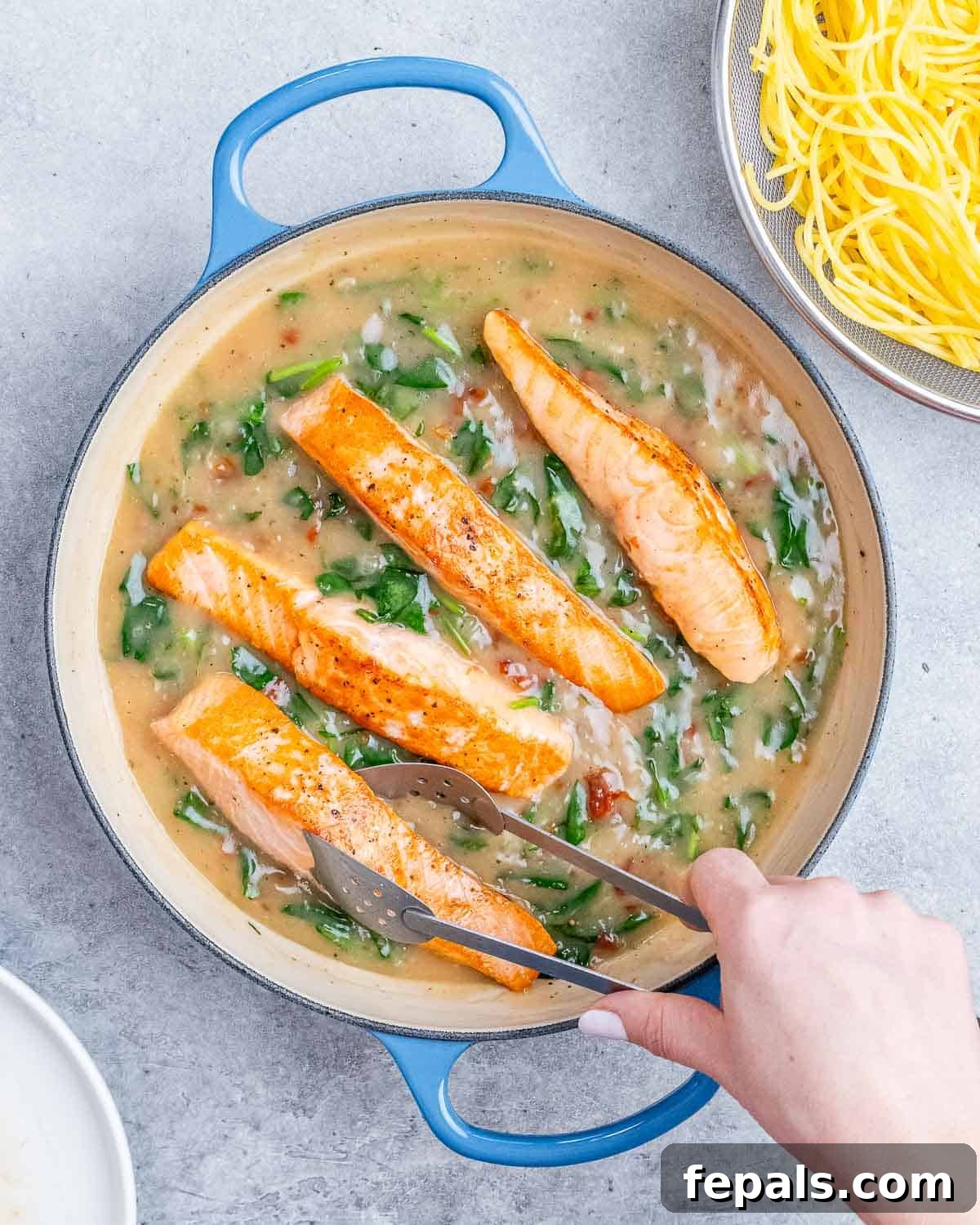 Decadent Salmon Alfredo 7 Adding salmon to a pot with a creamy spinach mixture.