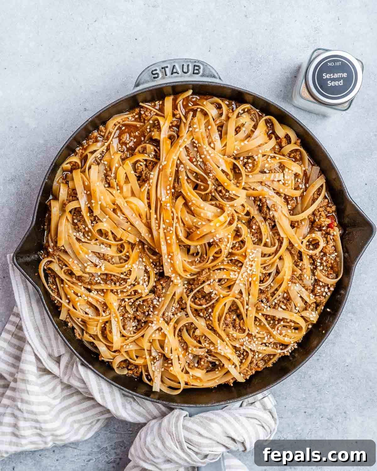 Beef and noodles in a black skillet, garnished with fresh green onions and sesame seeds.
