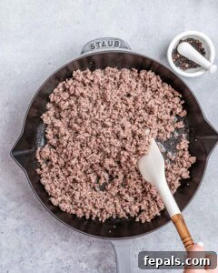 A spatula stirring ground beef in a skillet.