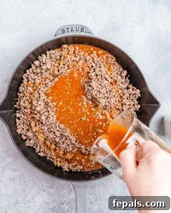 Pouring sauce over ground beef in a skillet.