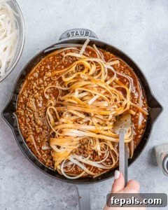 Tossing noodles in a beef sauce in a skillet with tongs.