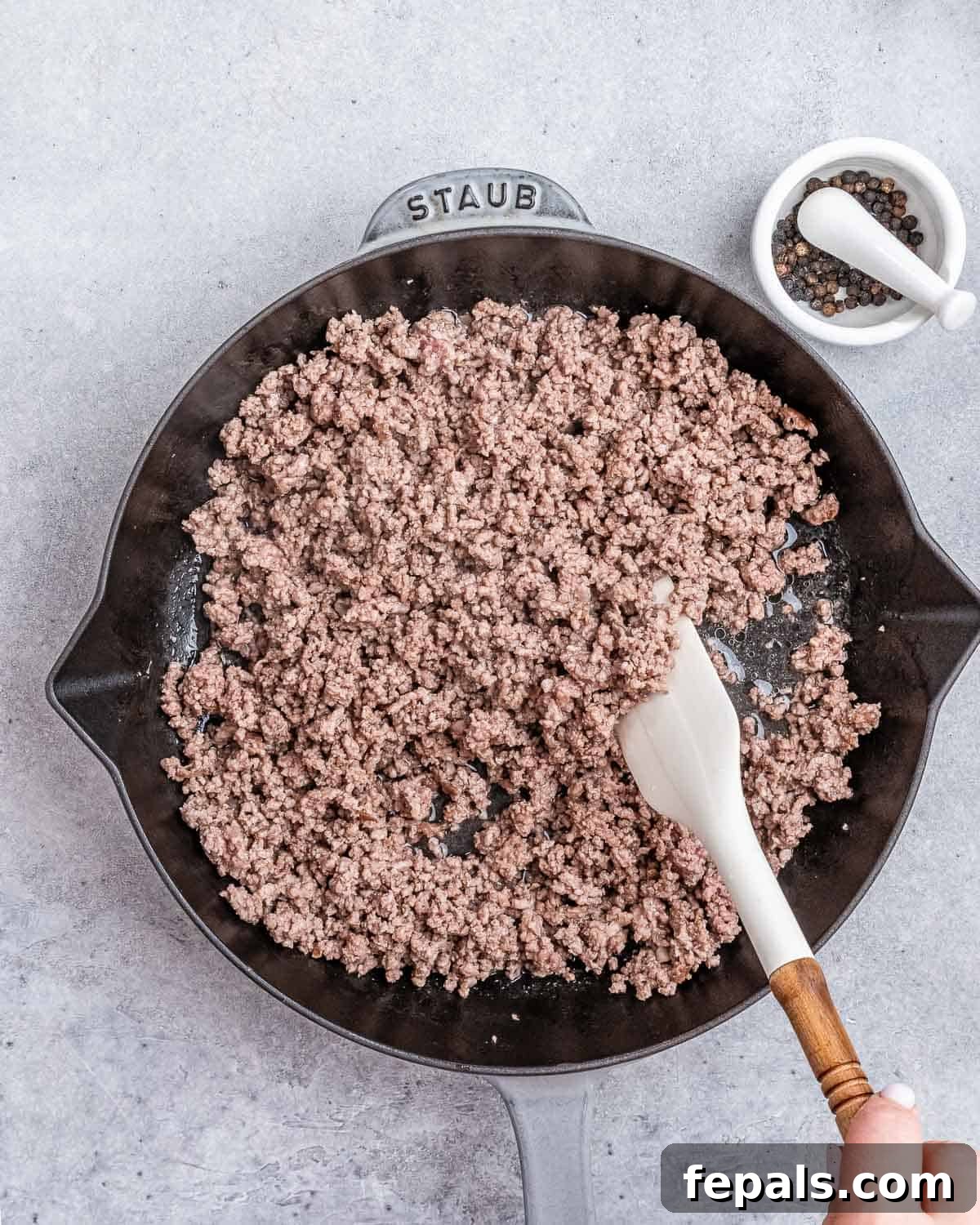 A spatula stirring ground beef in a cast iron skillet, ensuring even browning.