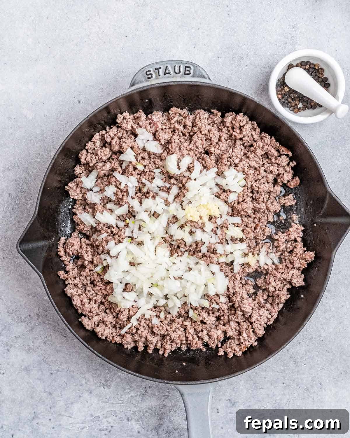Cooked ground beef in a skillet with finely chopped garlic and onion added, ready to be stir-fried.