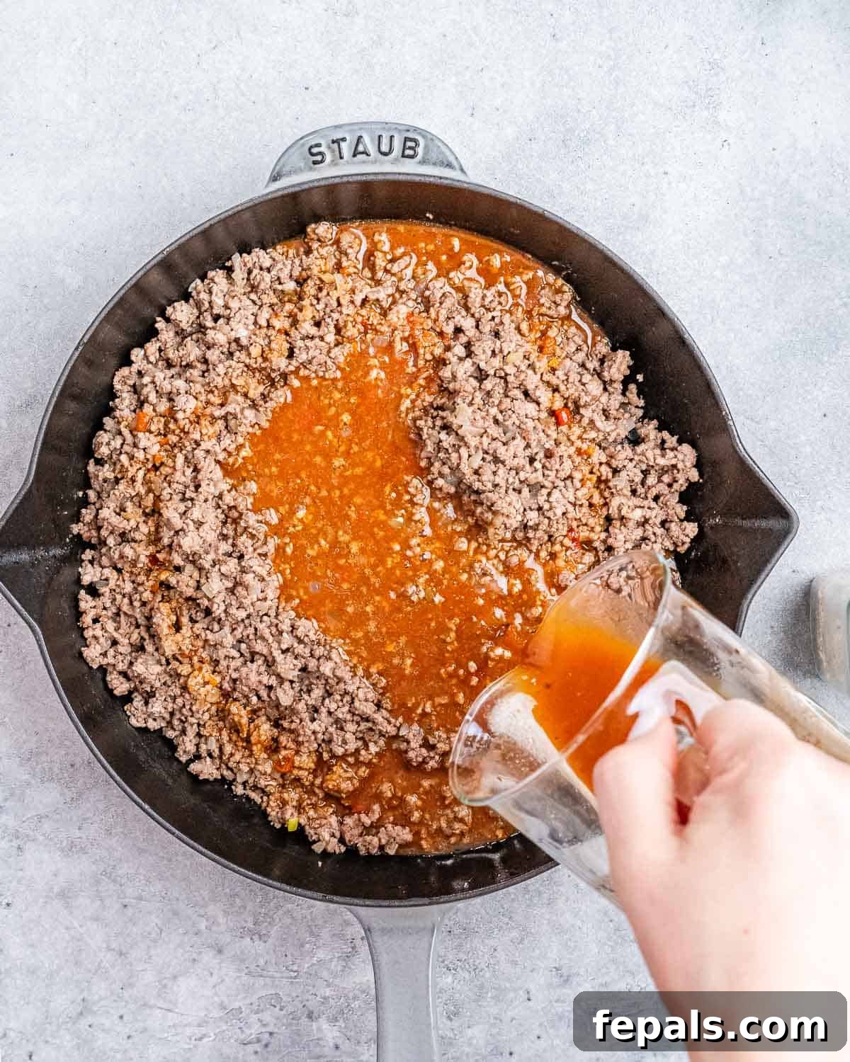 Rich, savory Mongolian sauce being poured over the browned ground beef in a skillet.