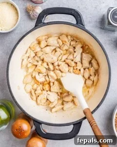 Stirring diced chicken in a pot with a white spatula.