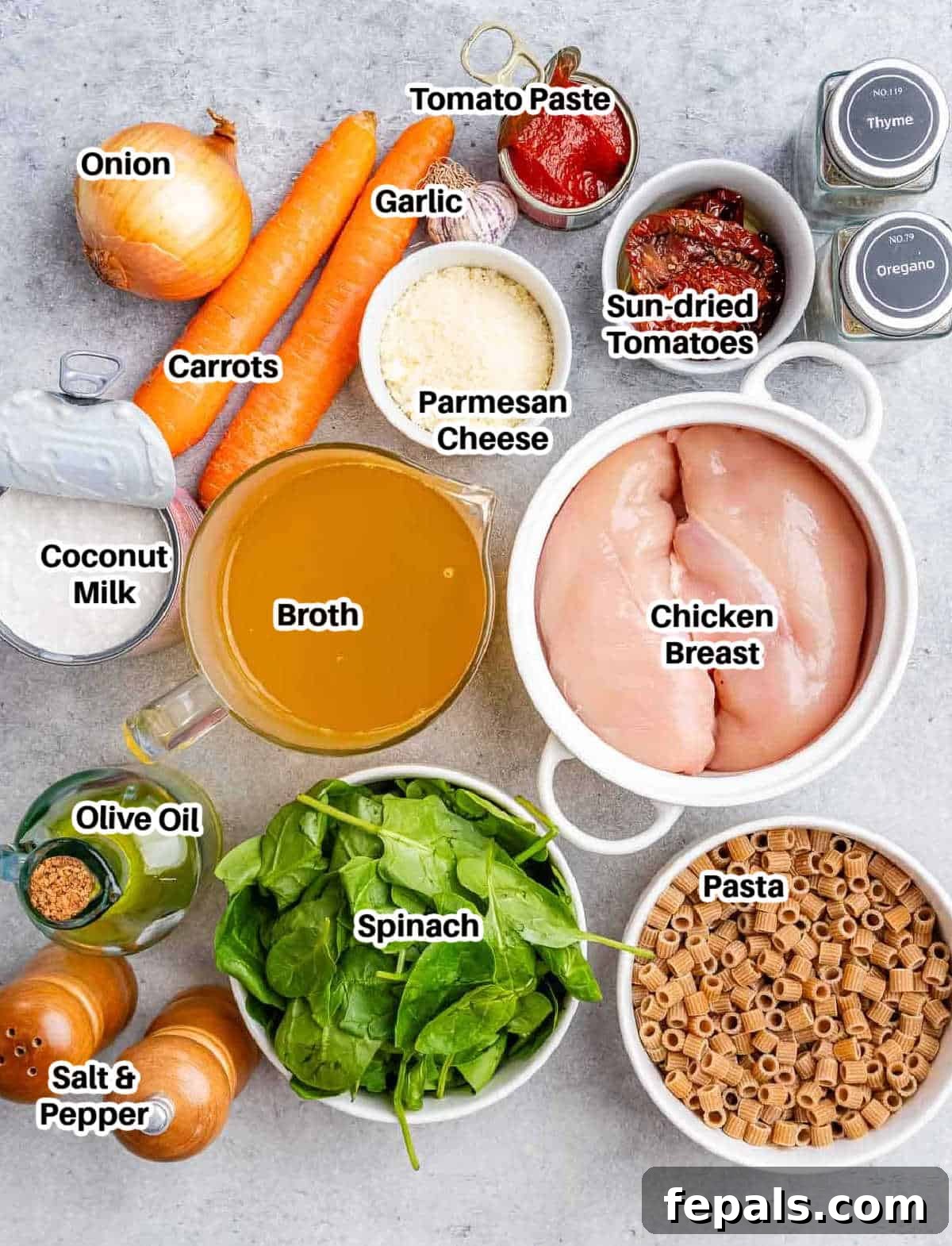 A flat lay of fresh ingredients to make marry me chicken soup including diced chicken, sun-dried tomatoes, spinach, garlic, onions, carrots, and herbs.