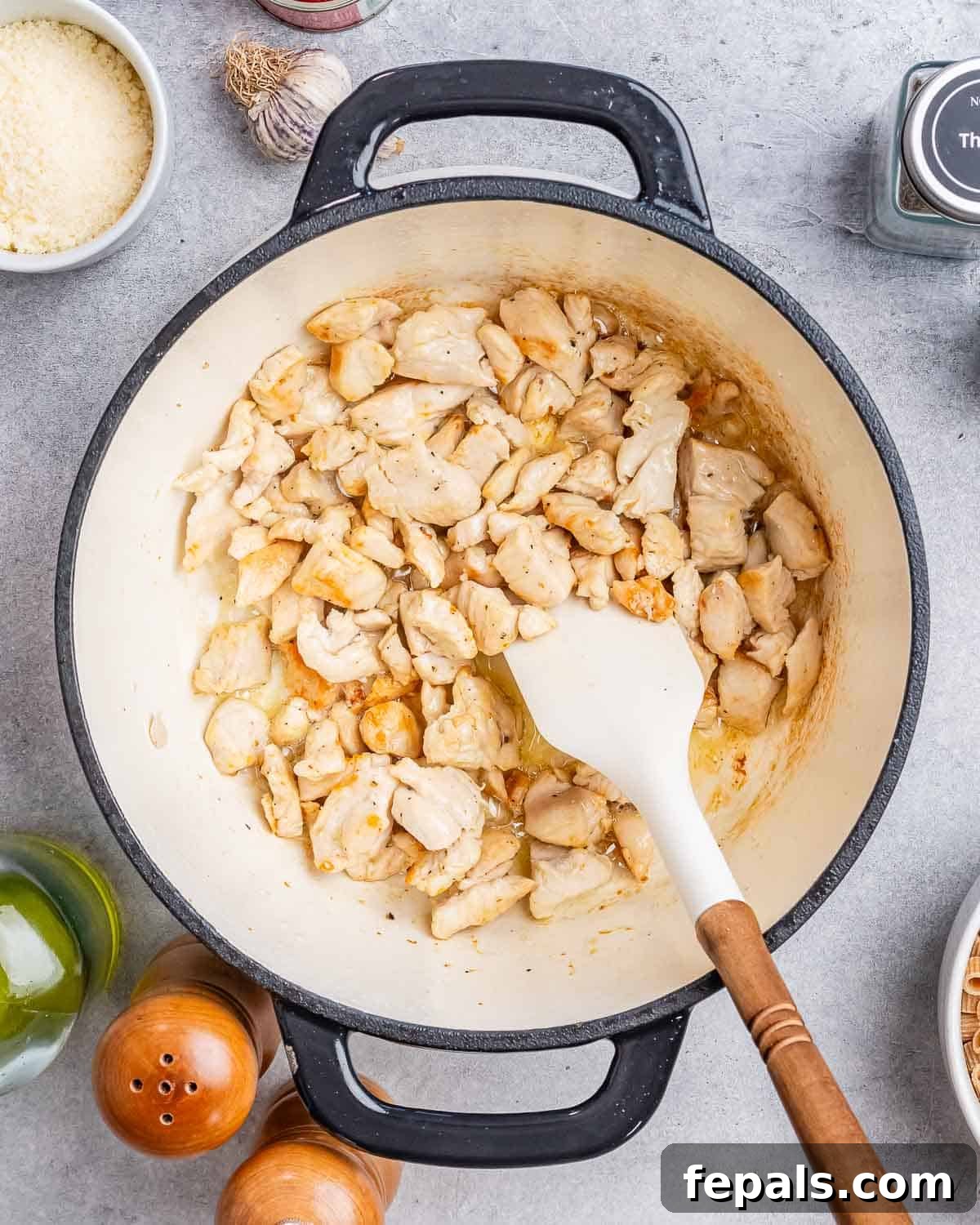 Stirring diced chicken in a large pot with a white spatula until no longer pink.