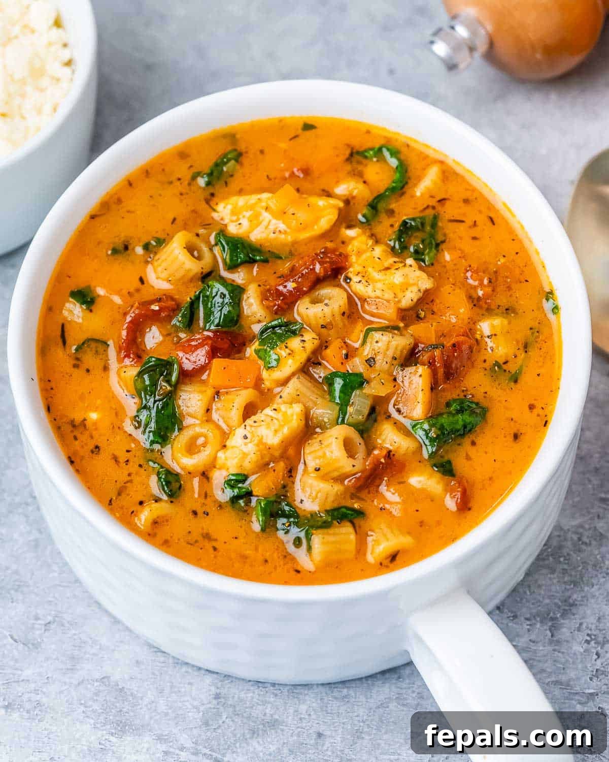 A white mug filled with creamy Marry Me Chicken Soup, garnished with fresh parsley, sitting on a gray surface.