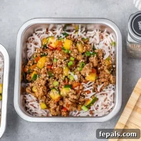 Meal prep container with fluffy white rice topped with savory ground turkey and mixed vegetables, garnished with fresh green onions.