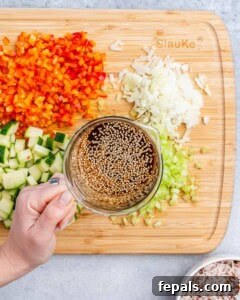 A hand holding a cup of liquid over a cutting board of chopped vegetables.