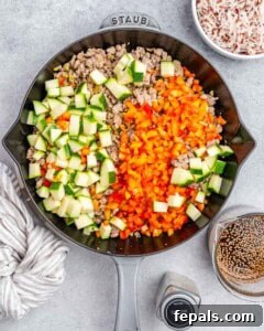 Brightly colored vegetables on top of ground turkey in a skillet.