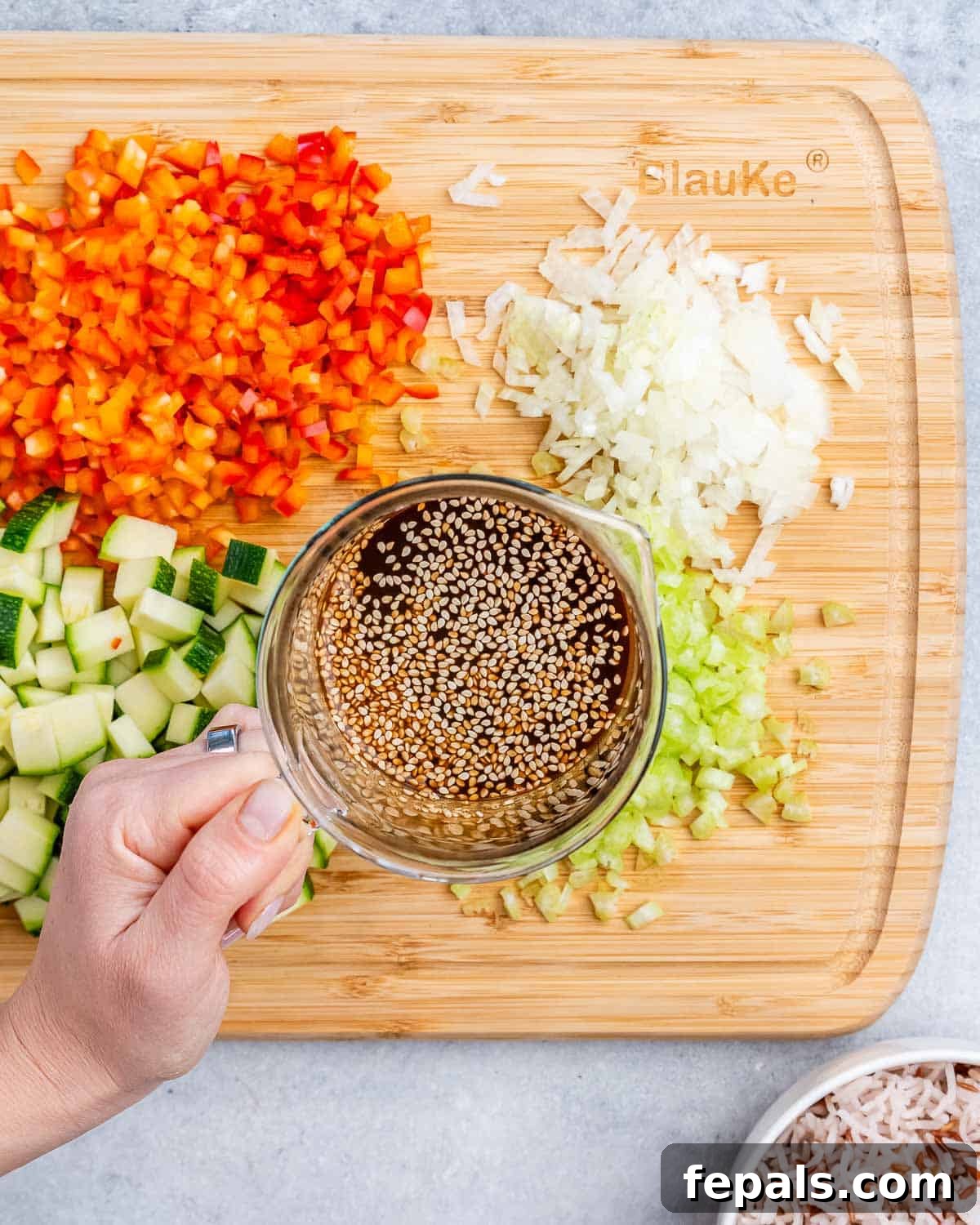 A hand holding a cup of liquid, representing the prepared stir fry sauce, positioned over a cutting board of freshly chopped vegetables.