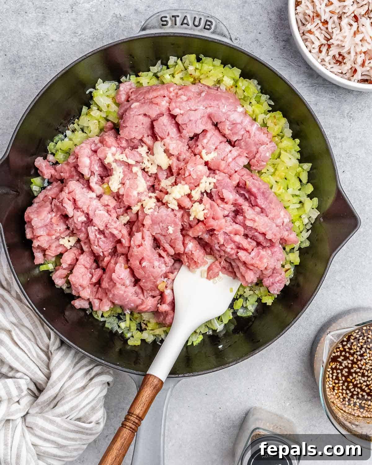 Raw ground turkey being stirred and broken apart with a white spatula in a skillet as it cooks and browns.