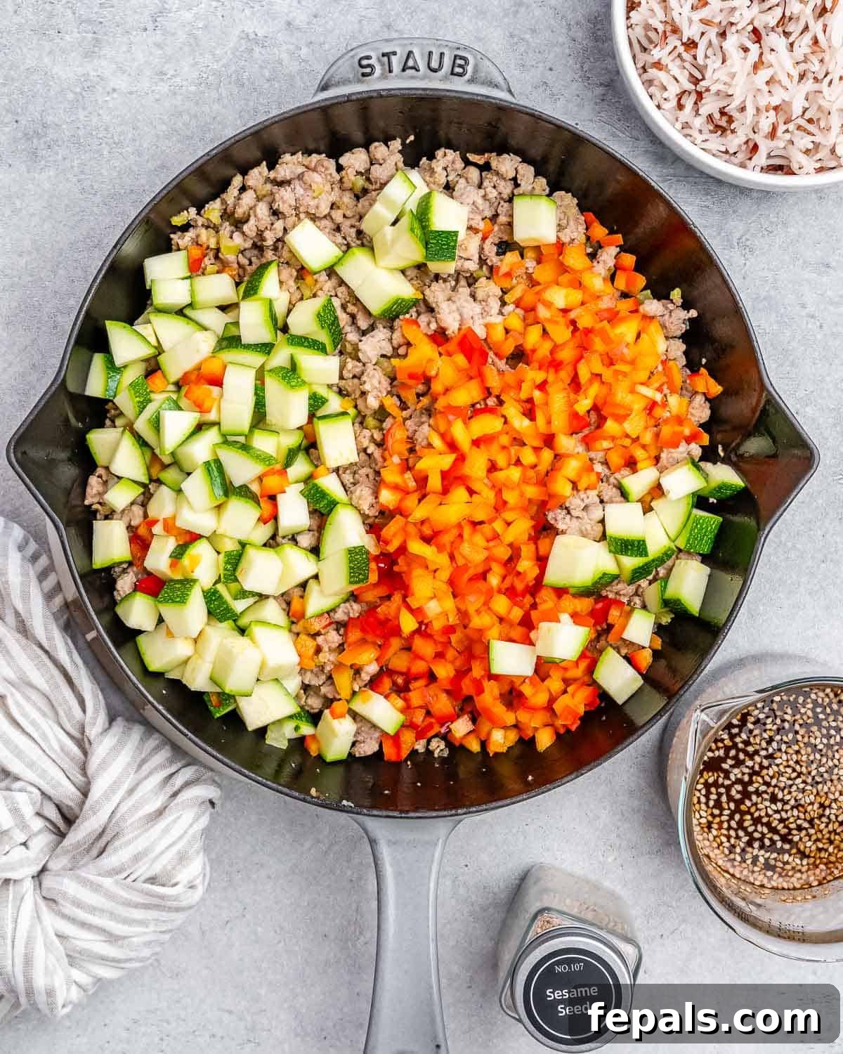 Brightly colored diced red bell pepper and zucchini added to the cooked ground turkey in a skillet, ready for stir-frying.