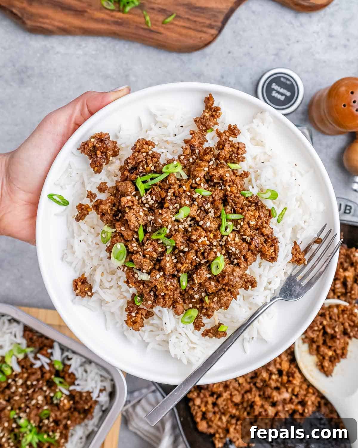Hearty Beef & Rice Medley 2 A hand holding a white plate with ground beef and rice with a fork on the side.