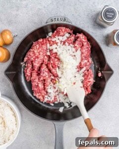 Hearty Beef & Rice Medley 13 A white spatula stirring onions and raw ground beef in a skillet.