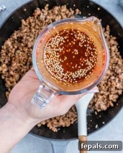 Hearty Beef & Rice Medley 15 A hand holding liquid over a skillet of ground beef.