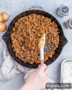 Hearty Beef & Rice Medley 16 Stirring ground beef in a skillet with a white spatula.