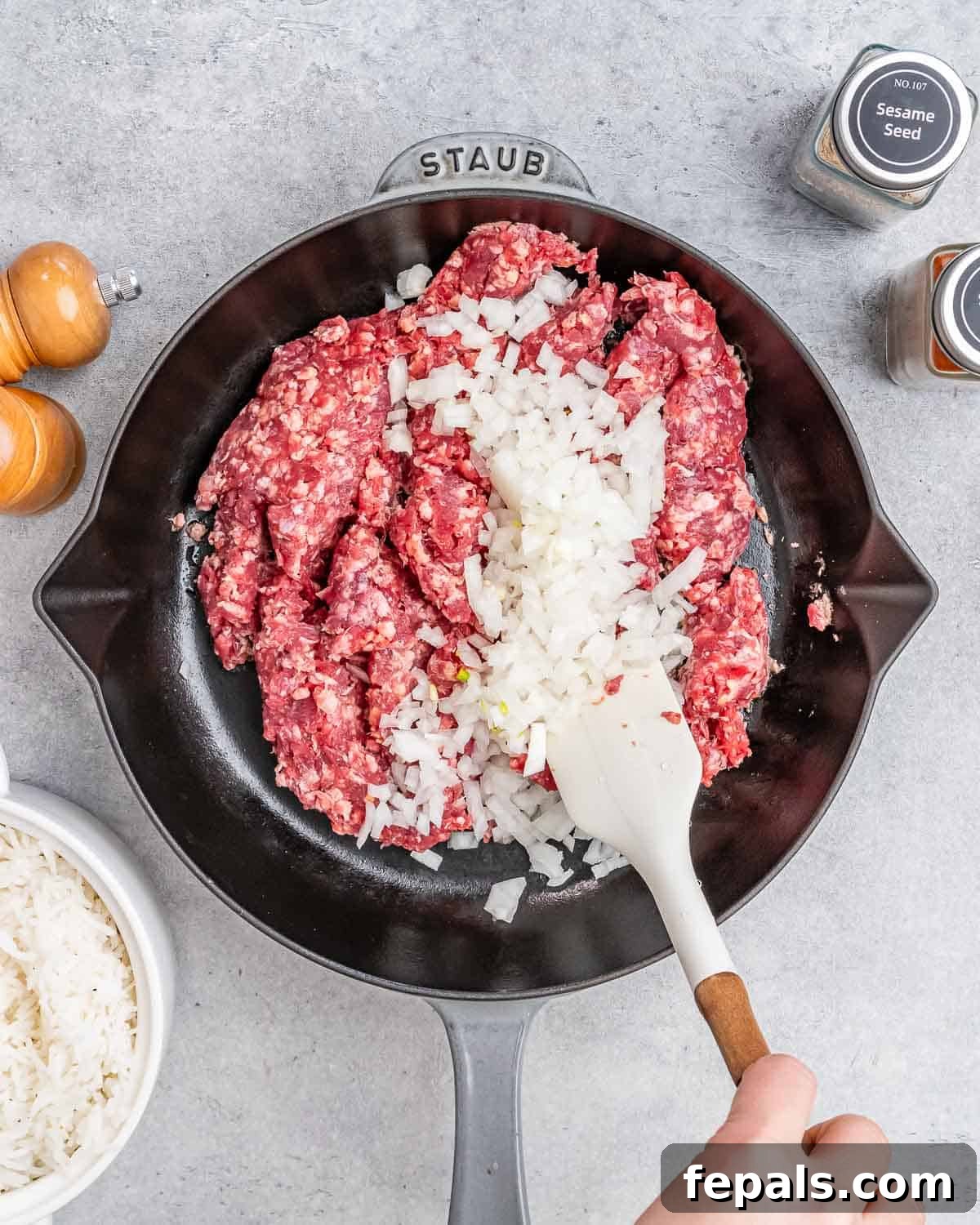 Hearty Beef & Rice Medley 5 A white spatula stirring onions and raw ground beef in a skillet.