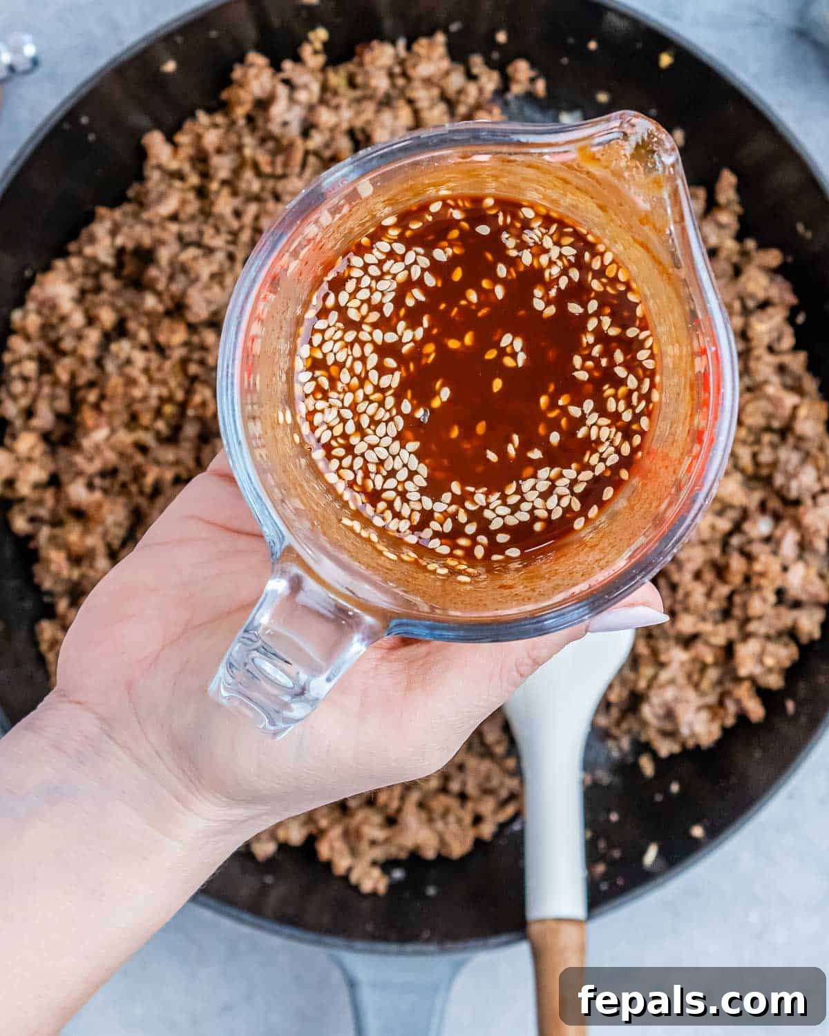 Hearty Beef & Rice Medley 7 A hand holding liquid over a skillet of ground beef.