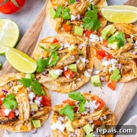 Chicken tostadas on a cutting board topped with cilantro and chopped avocados.