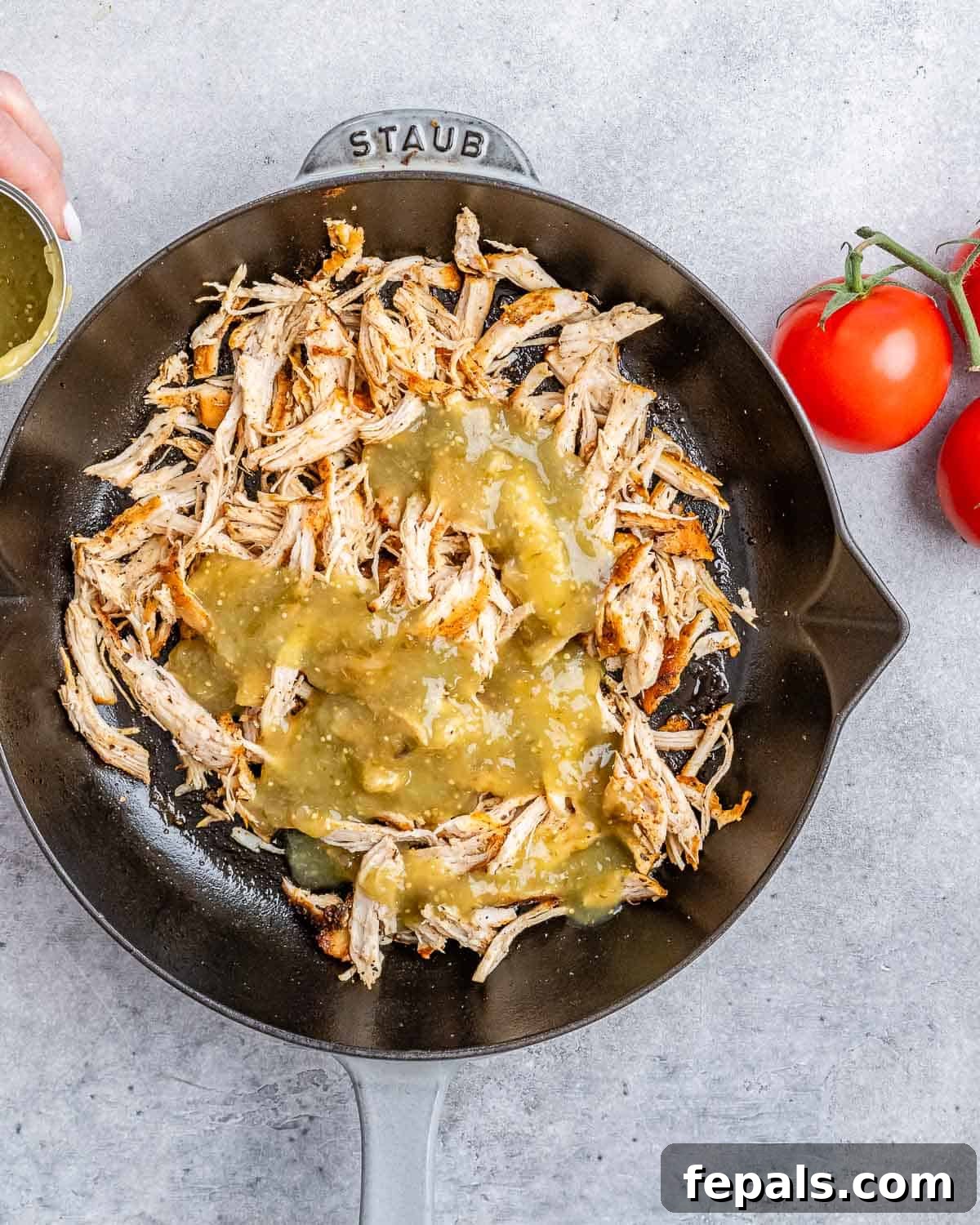 Fiesta Chicken Tostadas 5 Fluffy, shredded chicken coated in vibrant green salsa, simmering gently in a cast iron skillet, ready to top the tostadas.