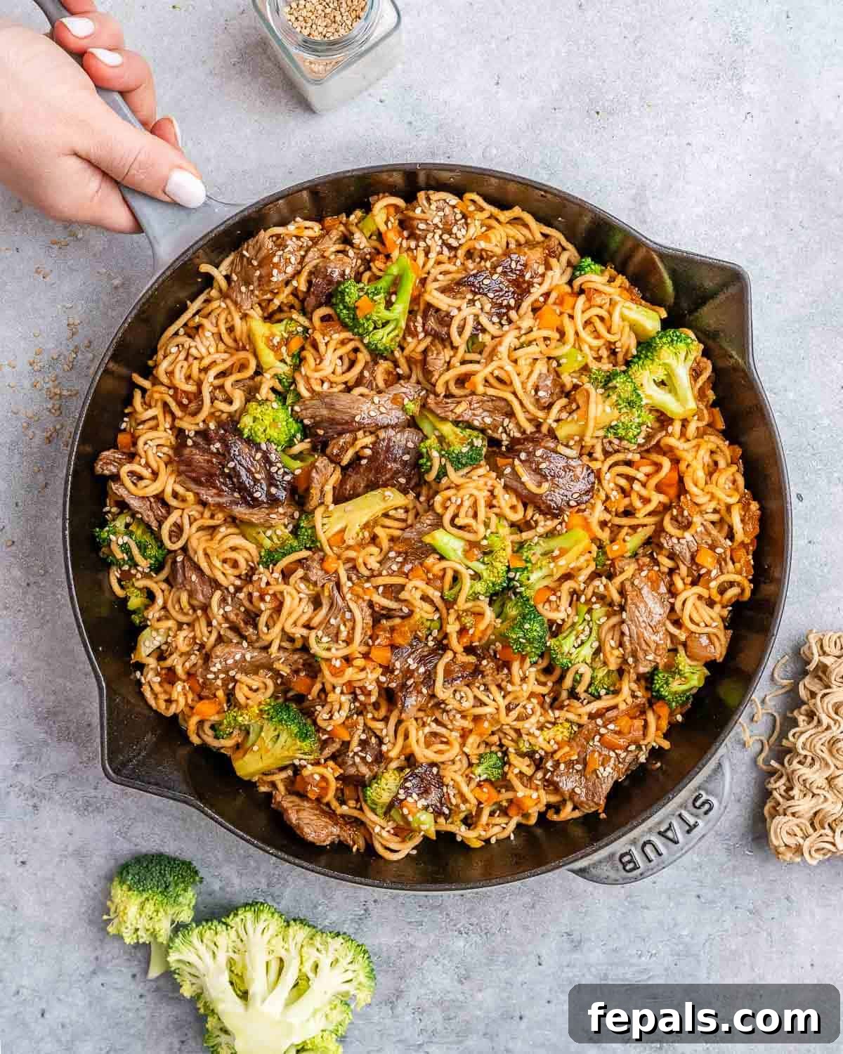 Wok-Tossed Beef Noodles 2 Beef lo mein in a cast iron skillet on a gray background, garnished with sesame seeds.