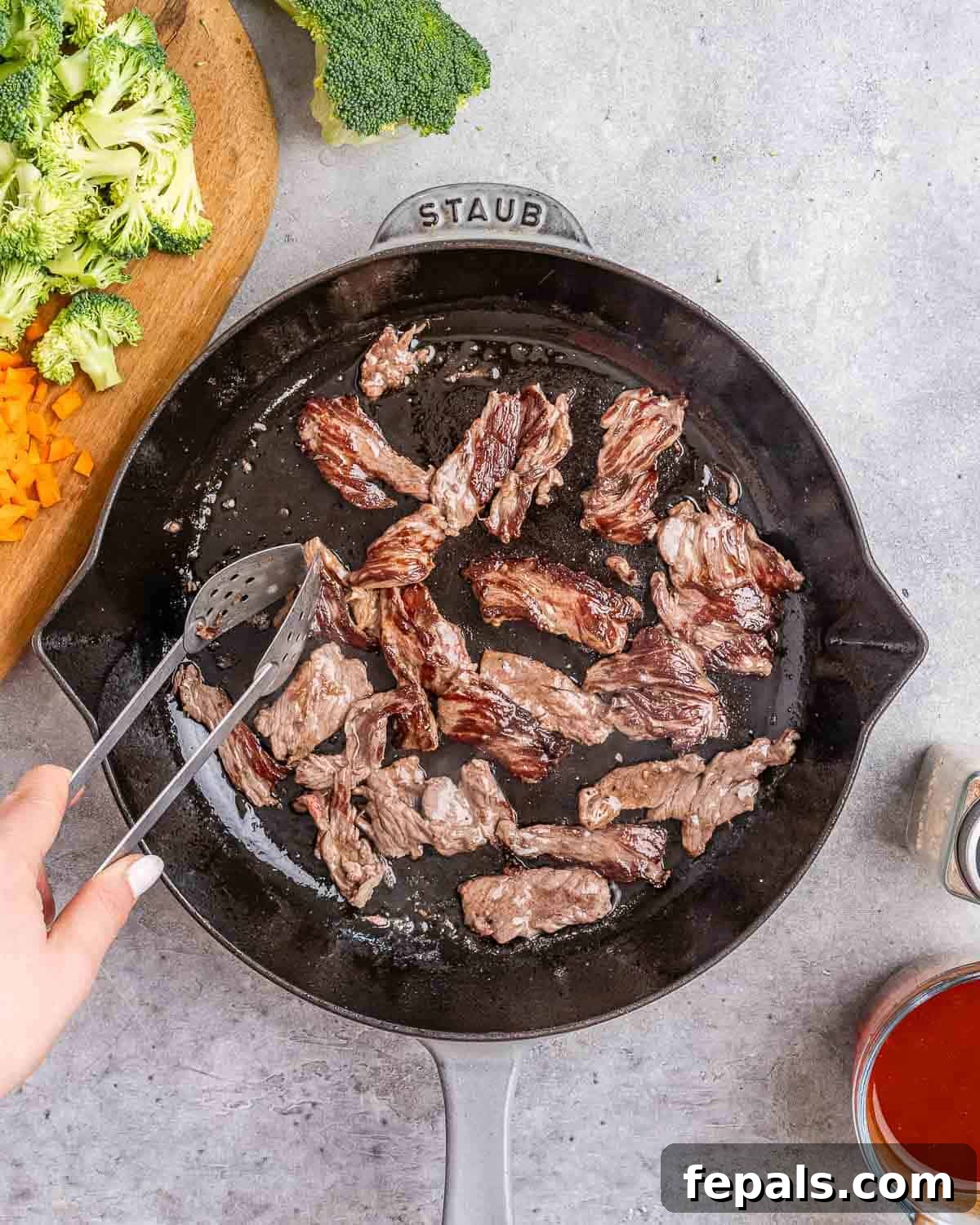 Wok-Tossed Beef Noodles 5 Tongs flipping pieces of thinly sliced beef in a hot skillet until browned.