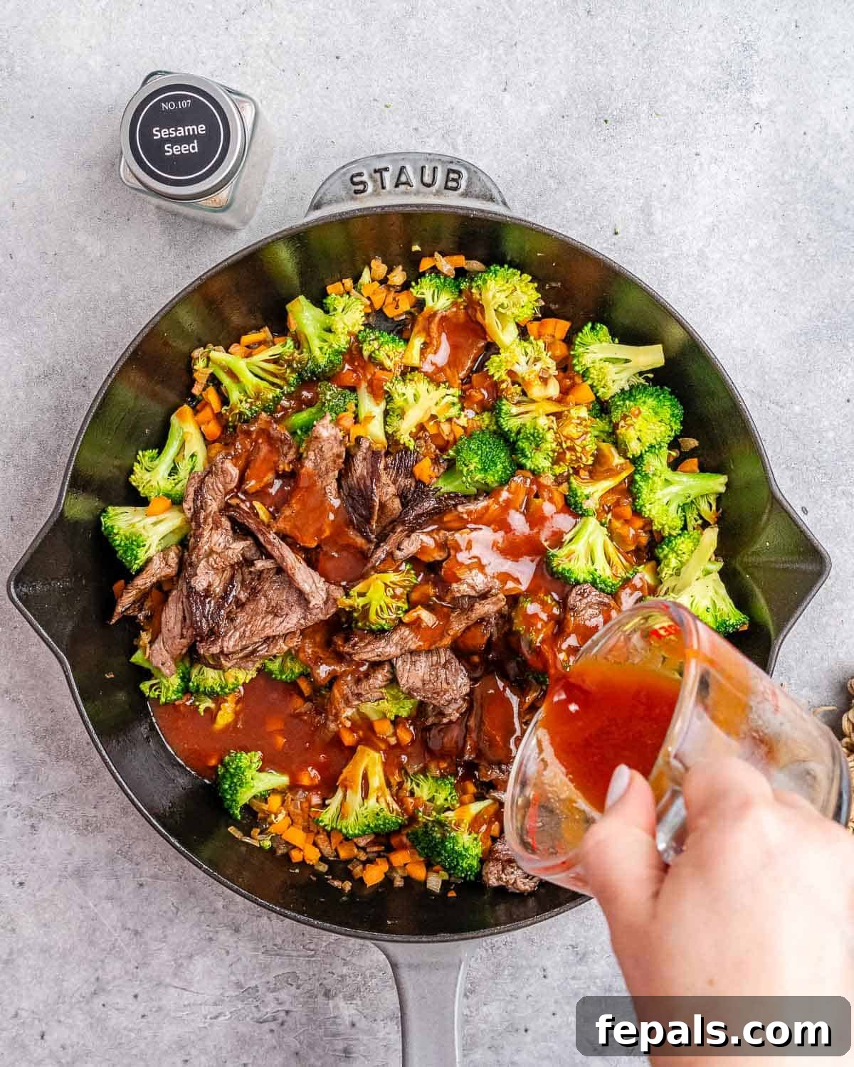 Wok-Tossed Beef Noodles 7 The prepared sauce being poured over the seared beef and stir-fried vegetables in a skillet.