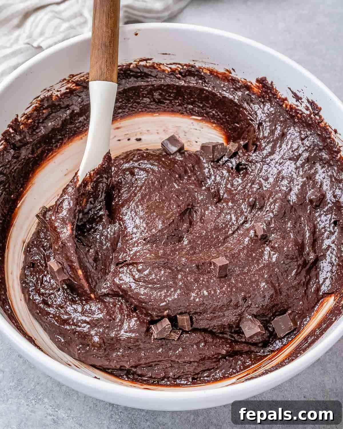 Fudgy Almond Flour Brownies 7 Chopped dark chocolate chunks being folded into the brownie batter in a white bowl.