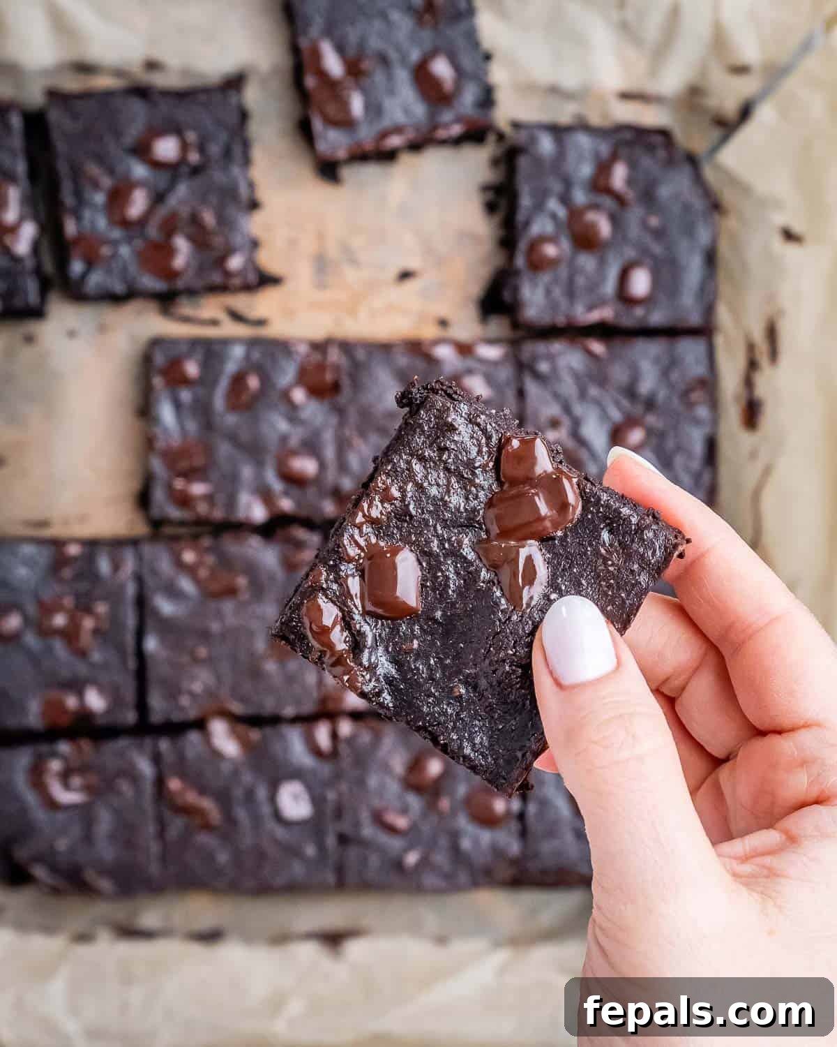 Fudgy Almond Flour Brownies 8 A hand holding a single fudgy brownie square, showcasing its dense texture, with more brownies in the background.