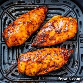 3 air fryer orange colored chicken breast in the air fryer basket.