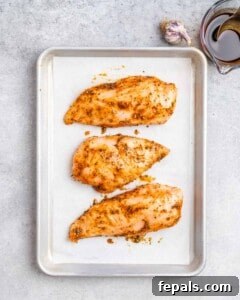 Three chicken breasts on a metal sheet pan.