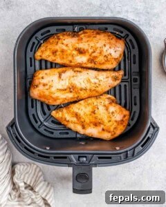 Three chicken breasts in an air fryer basket.