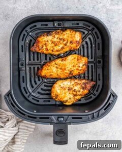 Three chicken breasts in an air fryer basket.