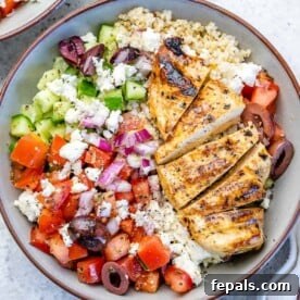 A top-down view of a colorful Greek chicken bowl, featuring grilled chicken, a fresh Greek-inspired salad, and fluffy quinoa, all nestled in a vibrant bowl.