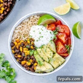A top-down view of a colorful vegetarian burrito bowl, richly filled with fluffy rice, tender beans, creamy avocado, ripe tomatoes, and a vibrant array of other fresh ingredients.