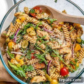 A clear, round bowl showcasing a vibrant chicken pasta salad, loaded with colorful vegetables and tender chicken pieces.