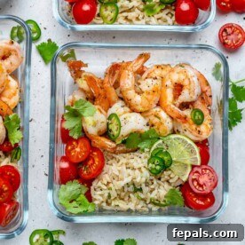 A vibrant meal prep bowl featuring perfectly sautéed shrimp and a side of fluffy brown rice, artfully topped with finely chopped tomatoes and fresh lime wedges, offering a burst of flavor and freshness.