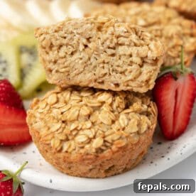 One-half muffin gracefully resting over a whole muffin on a plate, accompanied by a vibrant medley of sliced fruits, making for a wholesome breakfast.