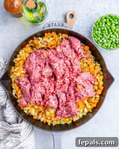 Homestyle Beef Shepherd's Delight 13 Raw ground beef over cooked veggies in a black skillet.