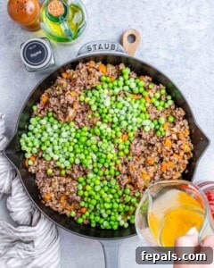 Homestyle Beef Shepherd's Delight 14 Pouring liquid from a measuring cup over beef and peas in a skillet.